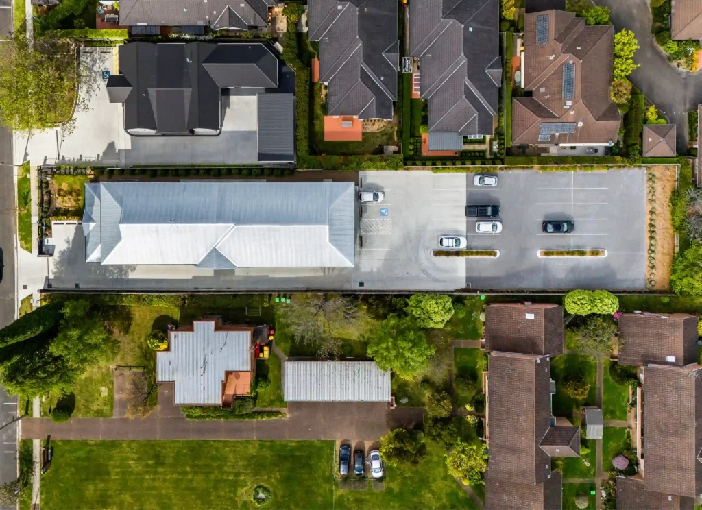 Aerial view of a commercial building and car park surrounded by suburban homes and greenery.