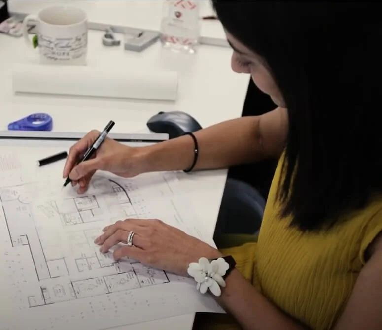 Woman marking up architectural floor plans with a pen at a desk.