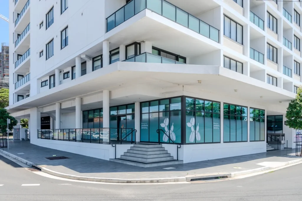 Modern apartment building with ground-floor commercial space and large glass windows on a street corner.